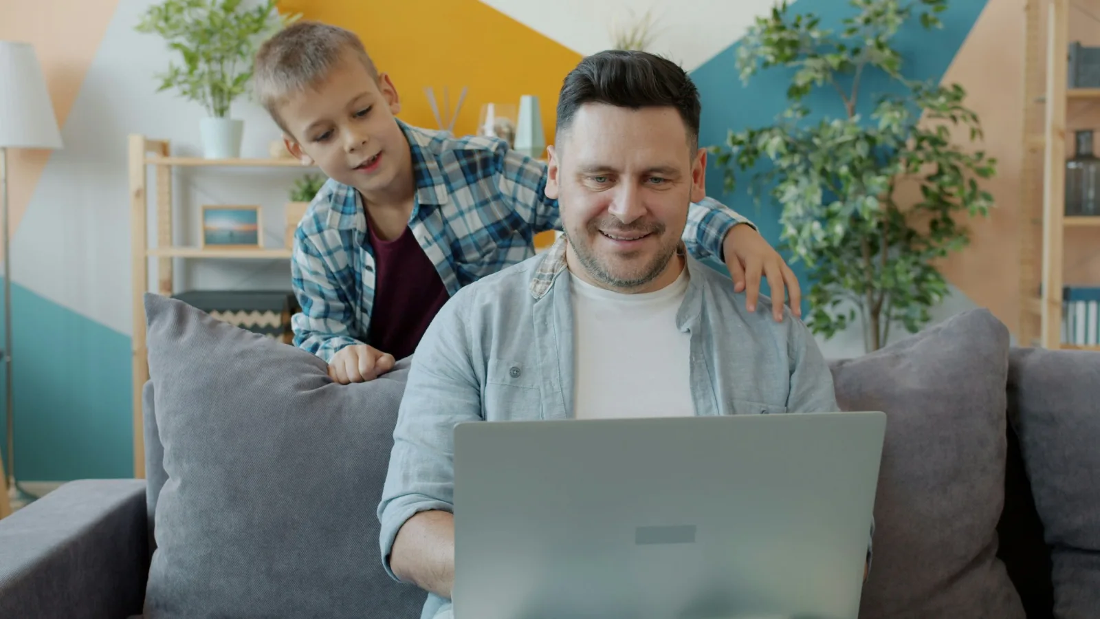 Vater und Sohn sehen gemeinsam auf einen Laptop in einem Wohnzimmer.